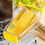 How to build credit fast - yellow credit card in a miniature shopping cart on a laptop, representing financial growth and credit score improvement in the usa.