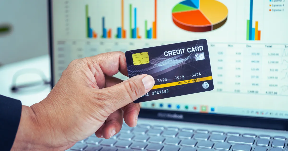 Amazing! Improve Credit Score to 750+ in 6 Months 2 A hand holding a credit card in front of a laptop displaying financial graphs, illustrating strategies to improve credit scores.