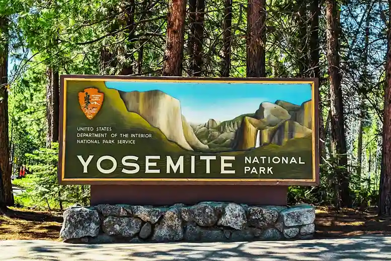 Entrance sign for Yosemite National Park surrounded by tall trees, symbolizing higher US national Parks Now Cost Triple shocking visitors