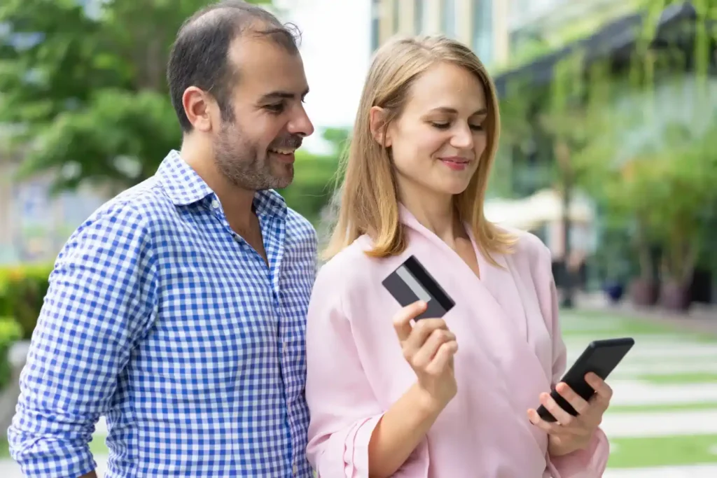 Woman holding EBT card and checking balance on smartphone outdoors