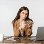 Woman counting cash while budgeting on laptop, how to save money fast on a low income