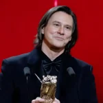 Jim Carrey holding award during ceremony, highlighting his net worth and Hollywood career success