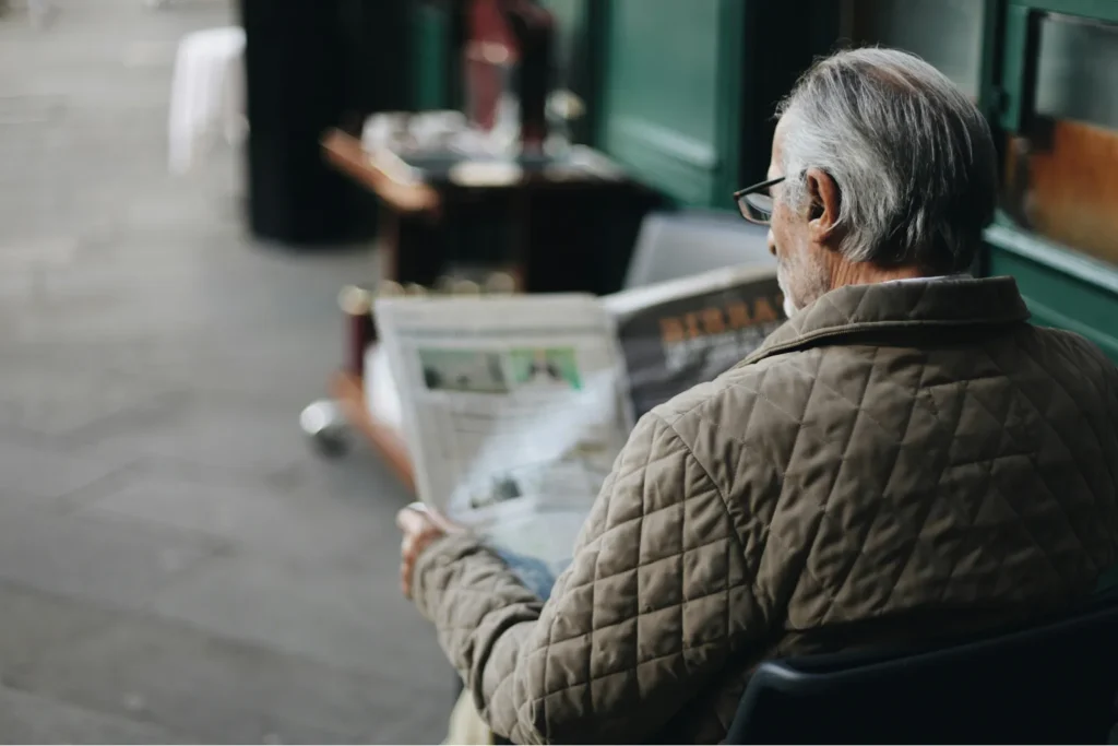 senior man reading newspaper about retirement planning and financial news while sitting outdoors